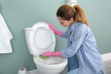 Photo of Woman cleaning toilet bowl in bathroom