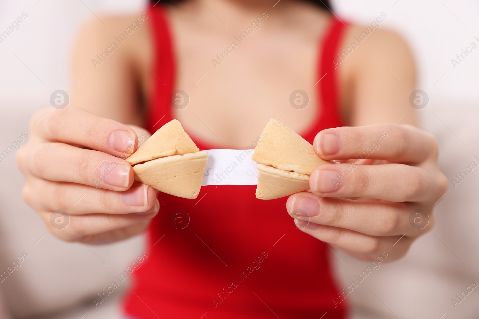 Photo of Young woman holding tasty fortune cookie with prediction indoors, closeup