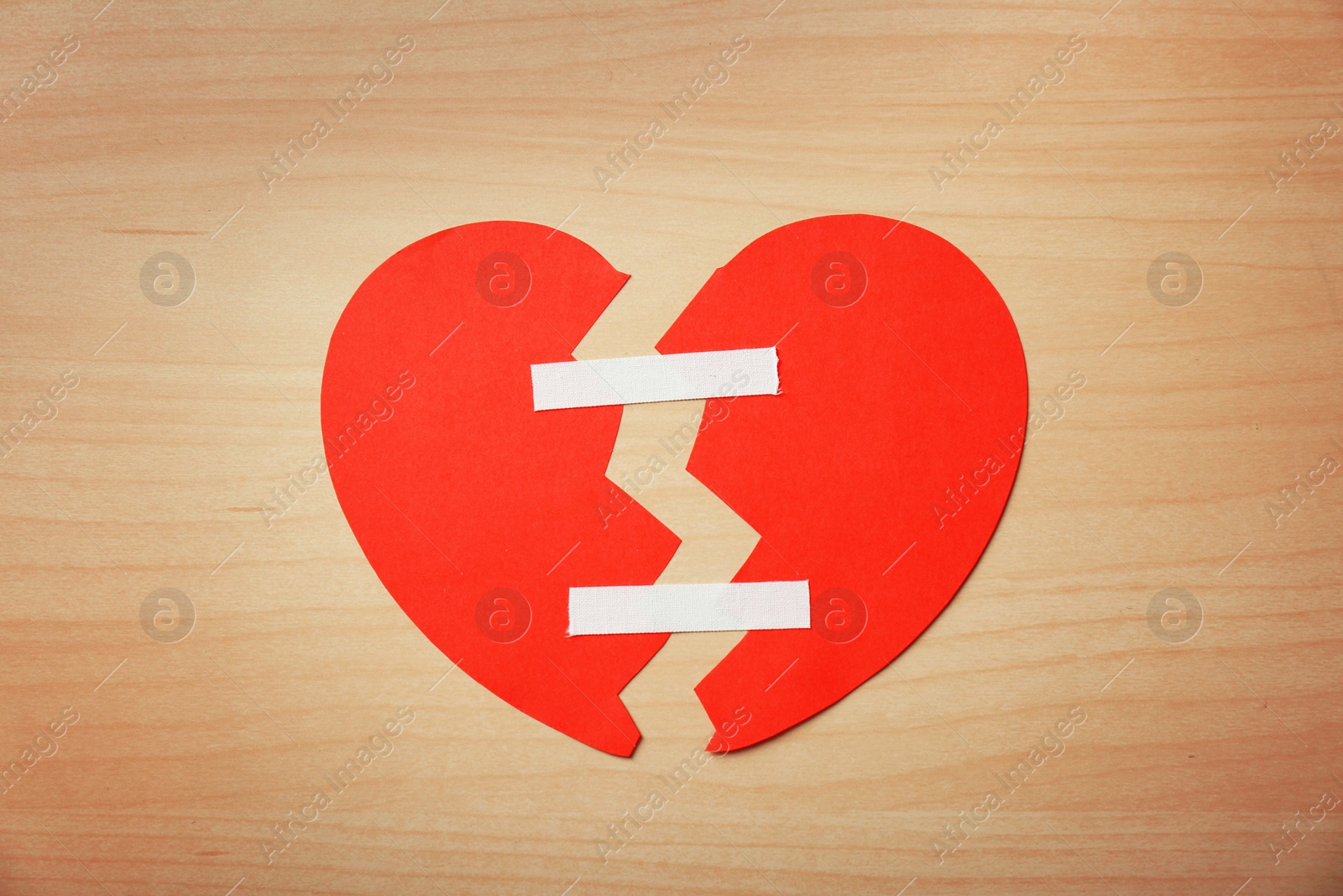 Photo of Halves of cut paper heart joined with adhesive plasters on wooden background, top view. Relationship problems