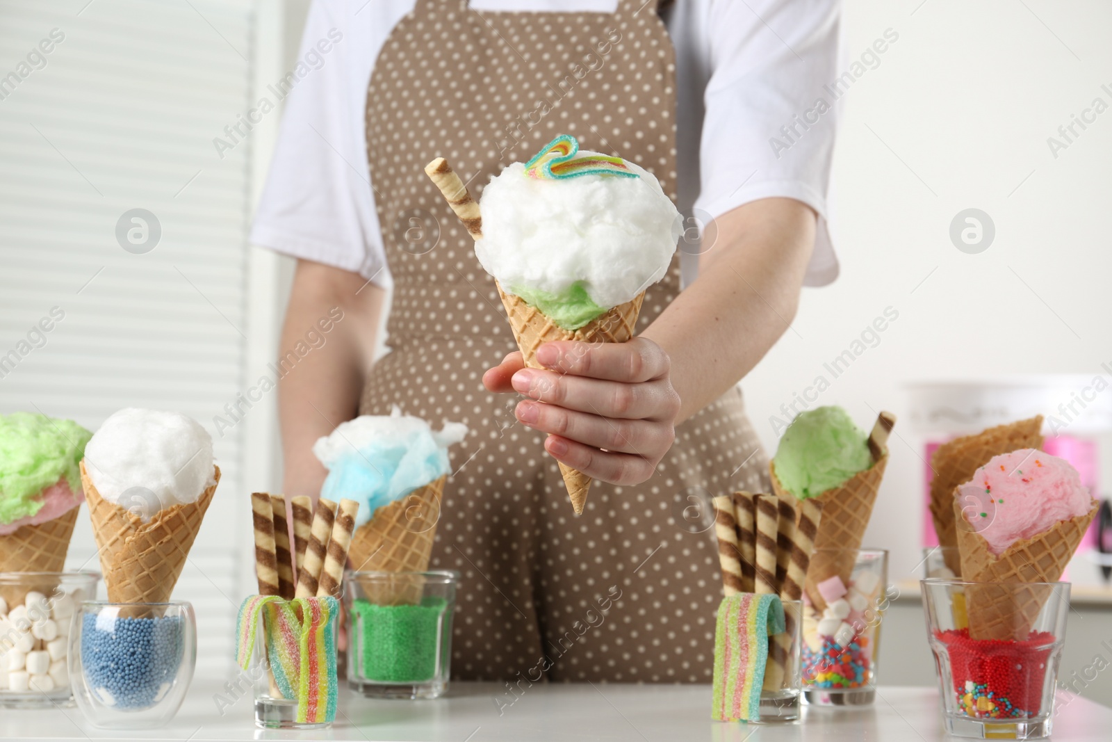 Photo of Woman holding waffle cone with cotton candy indoors, closeup