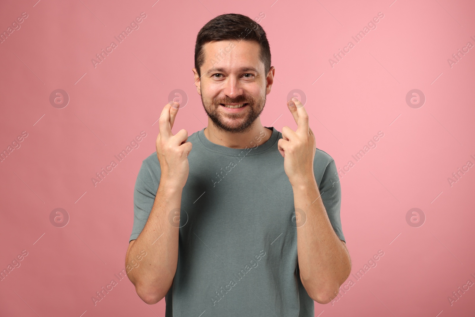 Photo of Happy man crossing his fingers on pink background