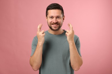 Photo of Happy man crossing his fingers on pink background