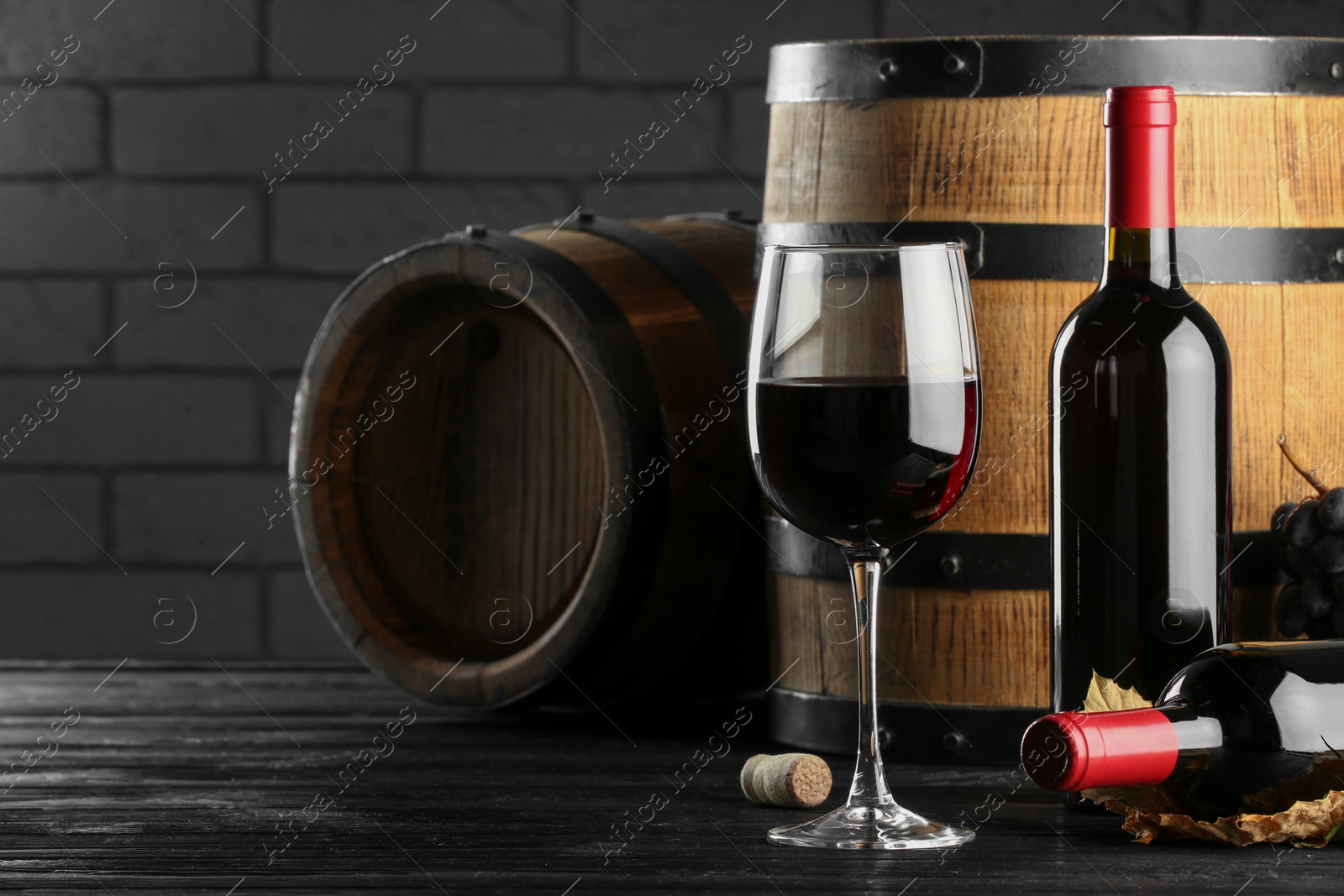 Photo of Delicious wine and wooden barrels on black table, space for text