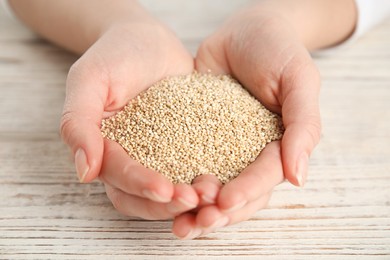 Woman with heap of white quinoa at wooden table, closeup