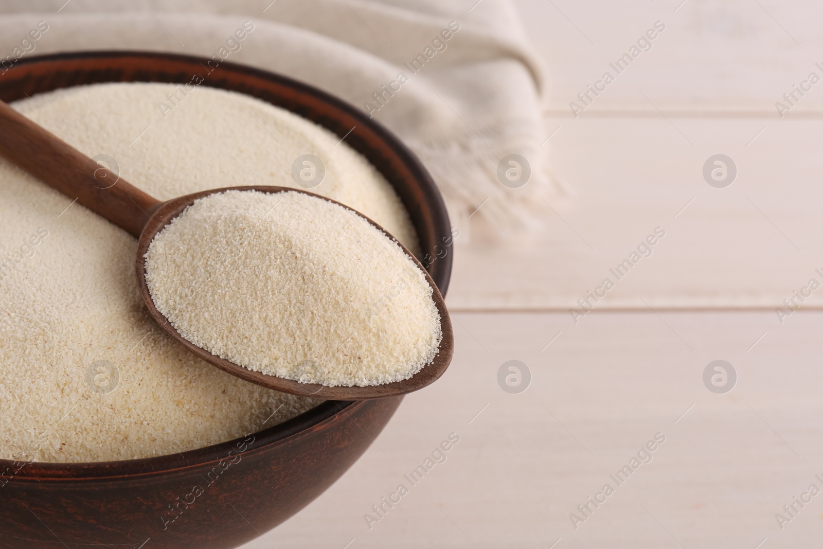 Photo of Uncooked organic semolina on white wooden table, closeup. Space for text