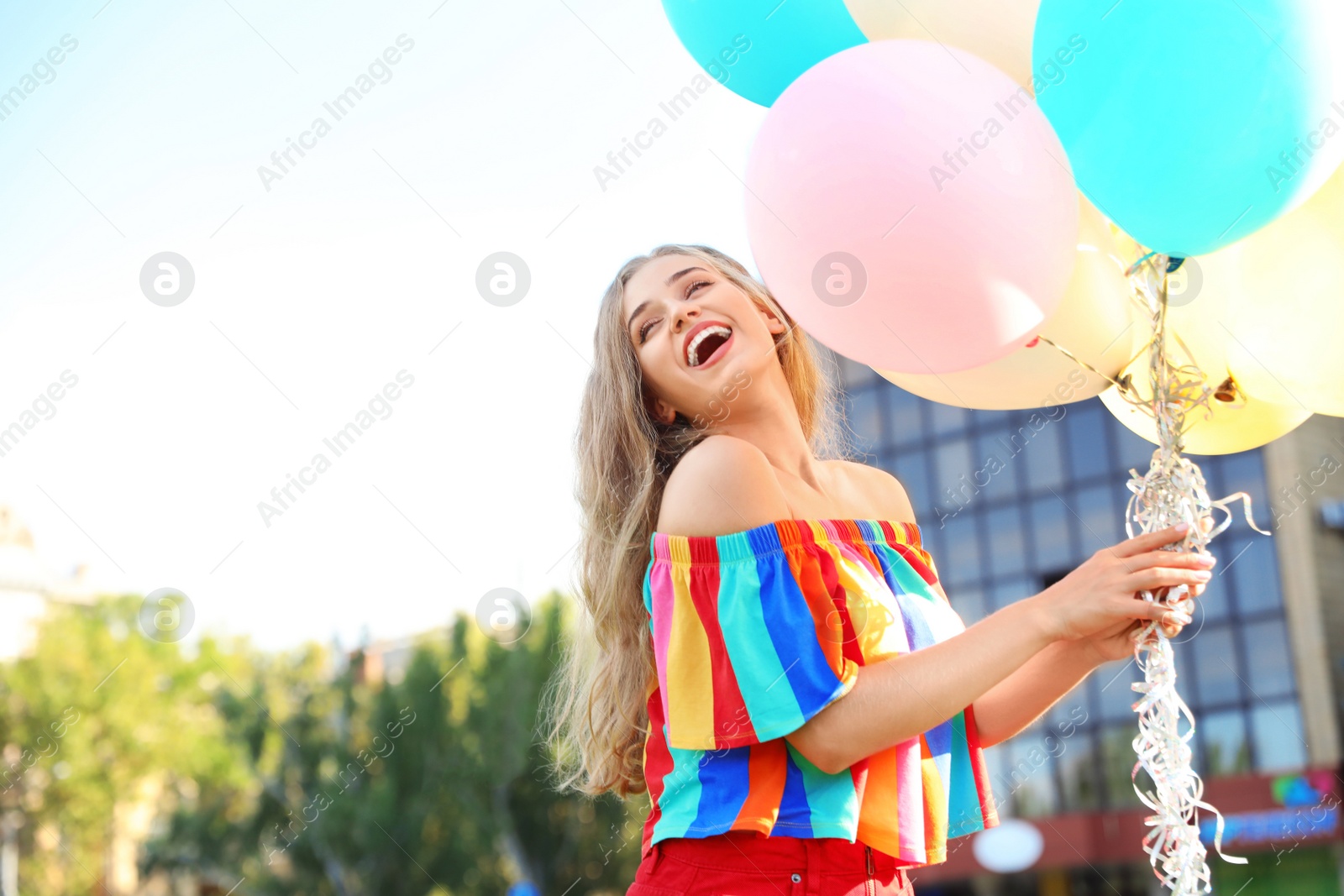 Photo of Beautiful young woman holding colorful balloons on street