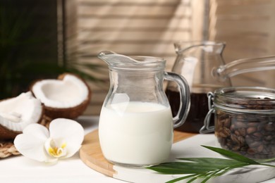 Glass jug of delicious coconut milk on white table indoors