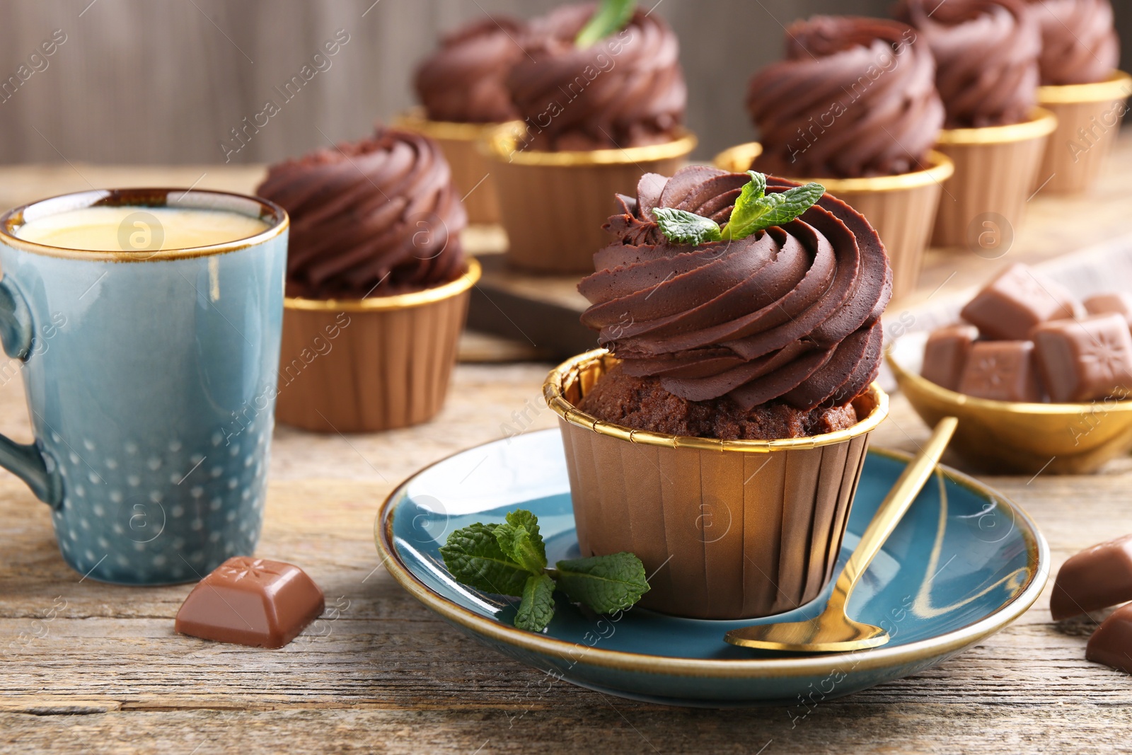 Photo of Delicious cupcakes with chocolate pieces and mint on wooden table