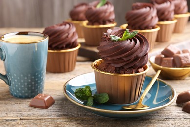 Delicious cupcakes with chocolate pieces and mint on wooden table