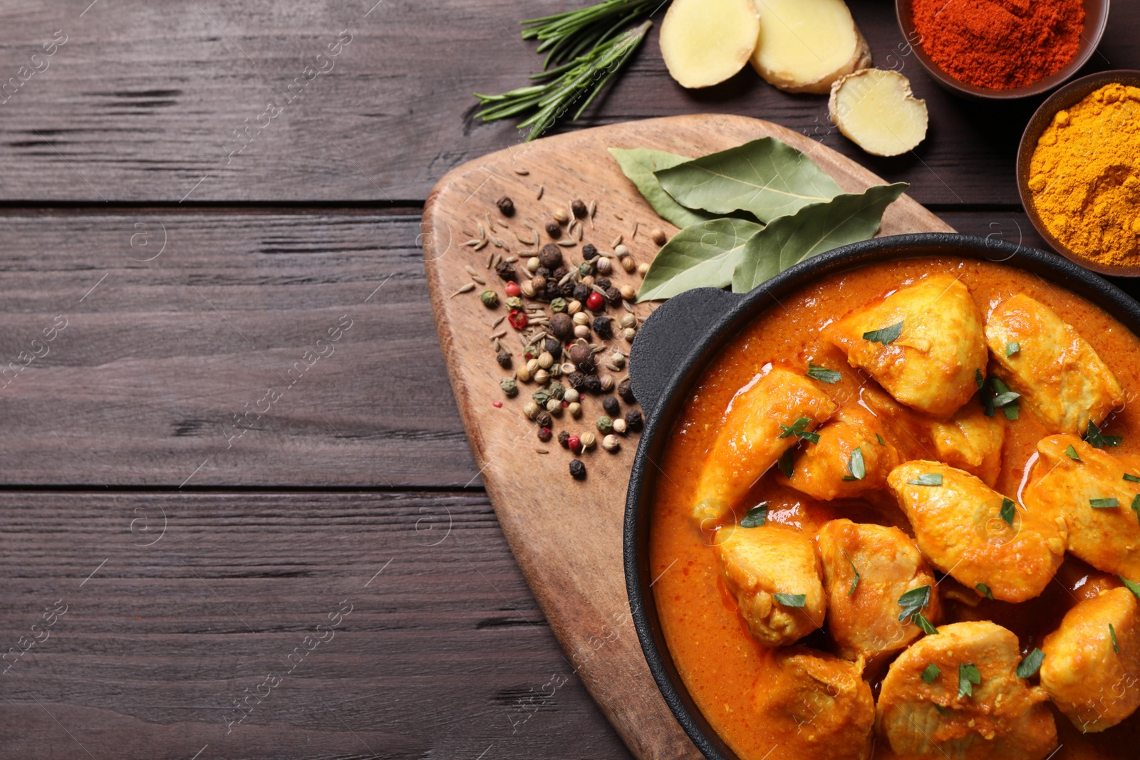 Photo of Delicious chicken curry in pan on wooden table, flat lay. Space for text