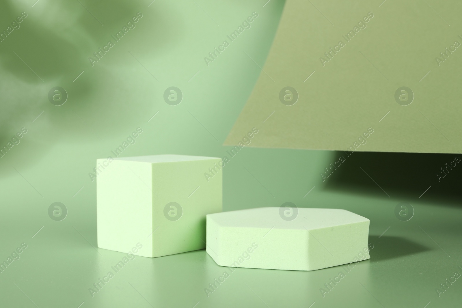 Photo of Presentation of product. Podiums, paper and shadows on green background. Space for text