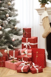 Photo of Many different gifts near Christmas tree and fireplace indoors