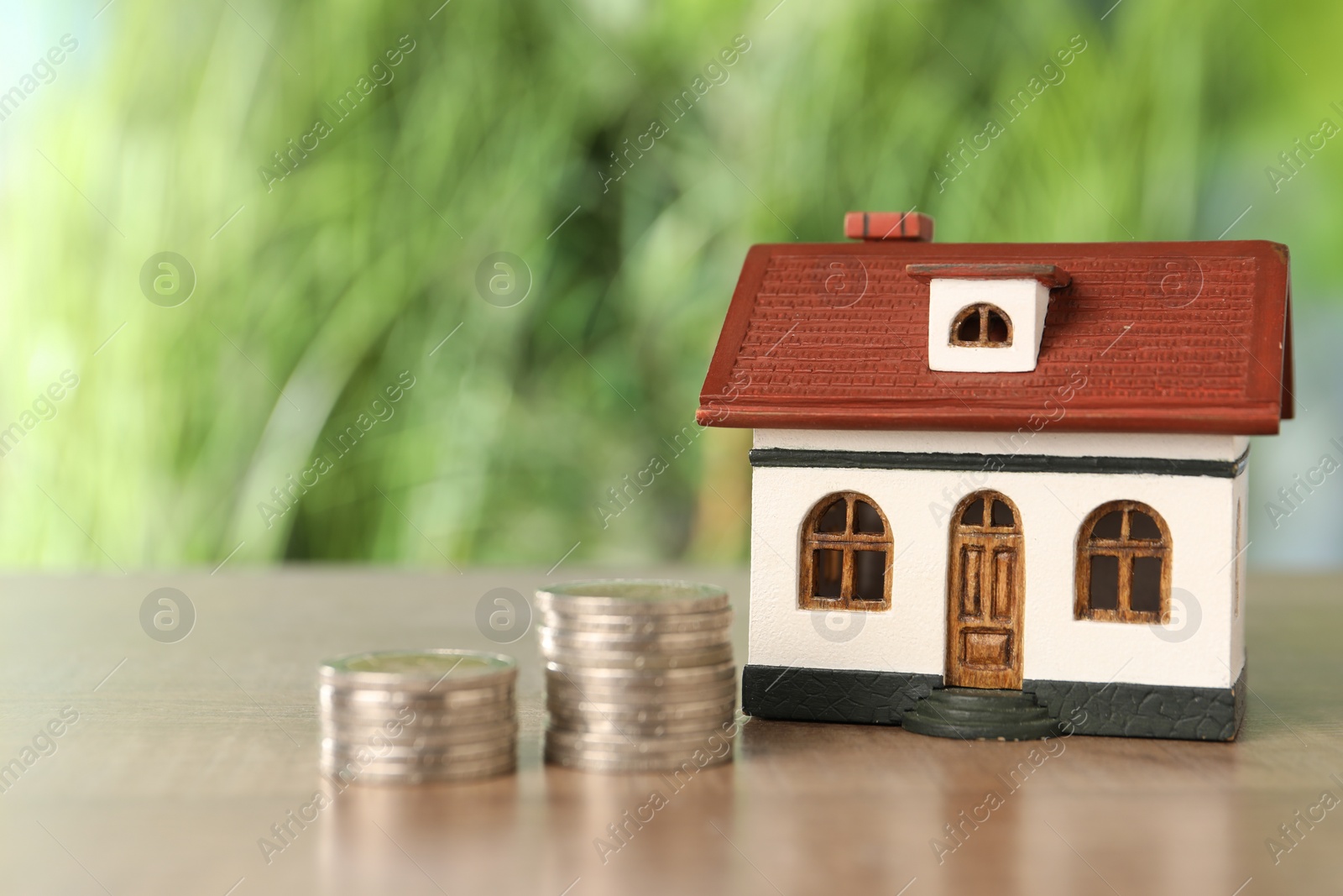 Photo of House model and stacked coins on wooden table outdoors