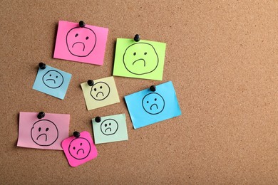 Photo of Many colorful paper notes with sad faces pinned to corkboard, space for text