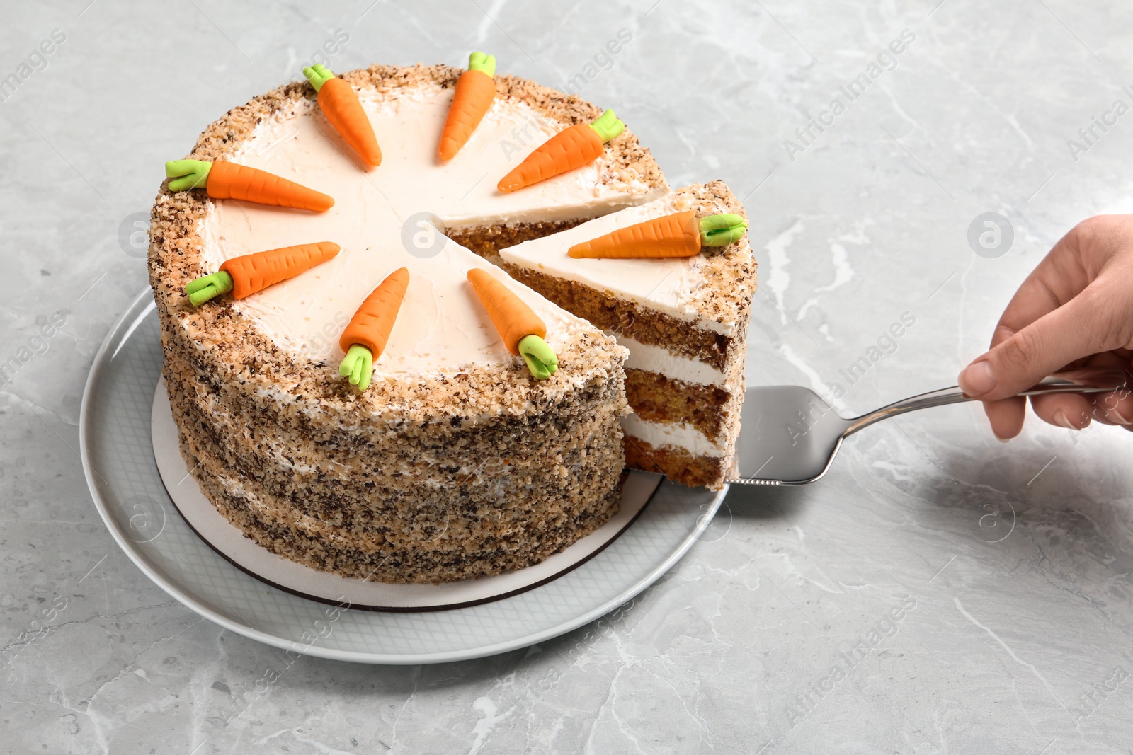 Photo of Woman taking piece of sweet carrot cake with delicious cream at grey marble table, closeup