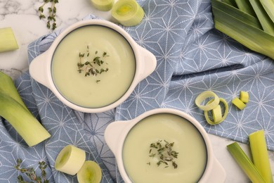 Photo of Tasty leek soup in bowls on white marble table, flat lay