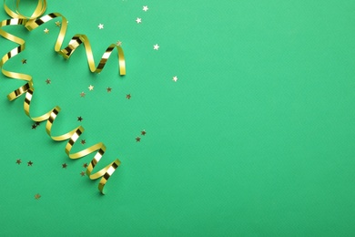 Photo of Shiny golden serpentine streamers and confetti on green background, flat lay. Space for text