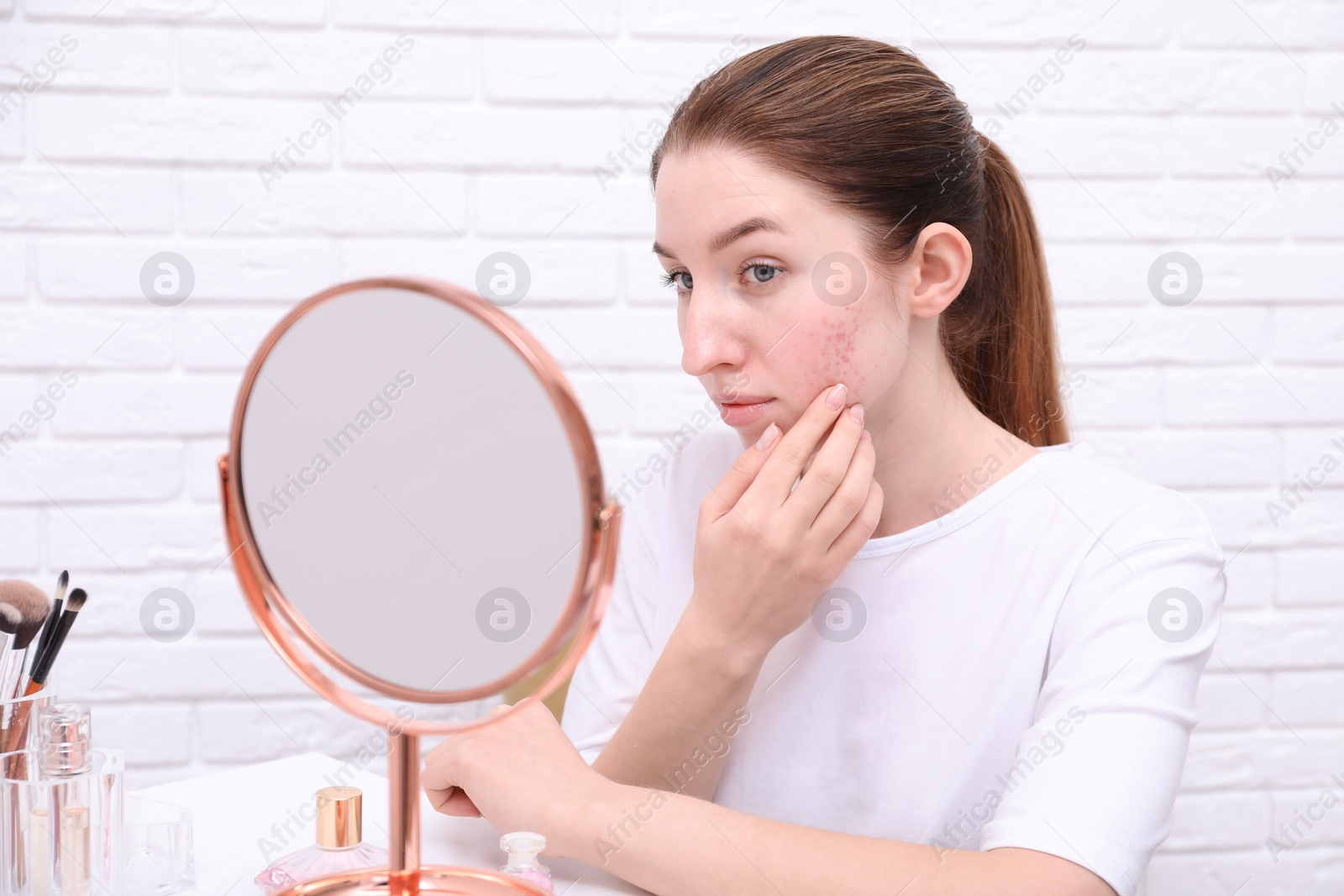 Photo of Woman with acne problem looking at mirror indoors