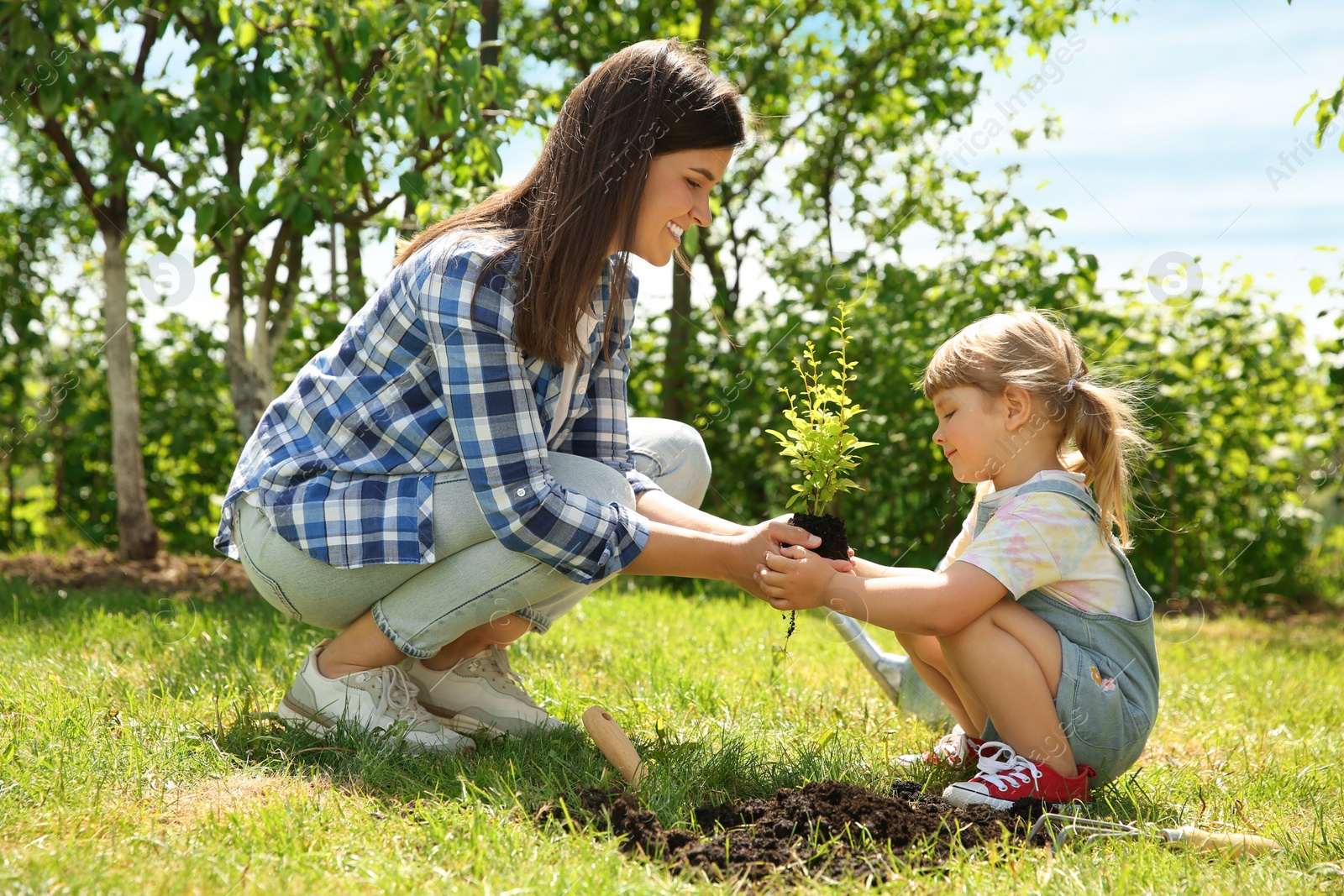 Photo of Mother and her daughter planting tree together in garden