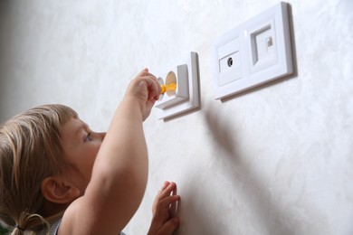 Photo of Little child playing with toy screwdriver and electrical socket at home, closeup. Dangerous situation