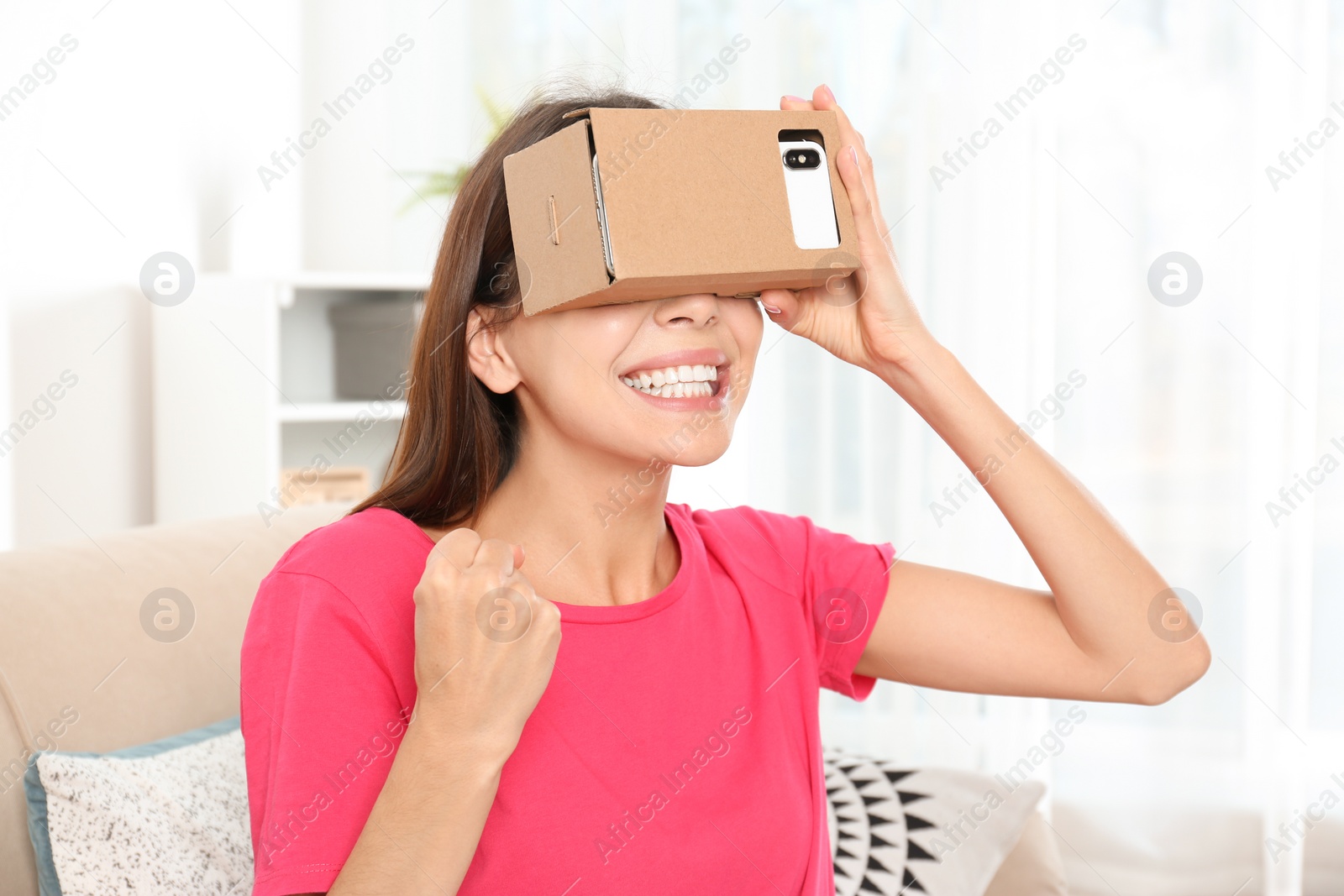 Photo of Young woman using cardboard virtual reality headset at home