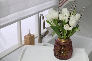 Photo of Beautiful bouquet of willow branches and tulips in vase near sink, space for text