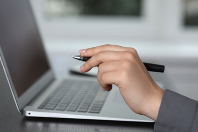 Photo of Woman with pen working on laptop, closeup. Electronic document management