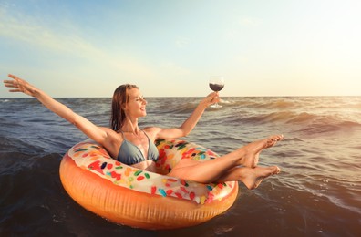Photo of Happy woman with glass of wine and inflatable ring in sea