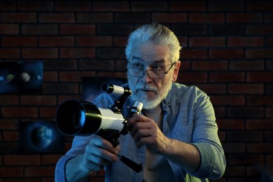 Senior man using telescope to look at stars in room