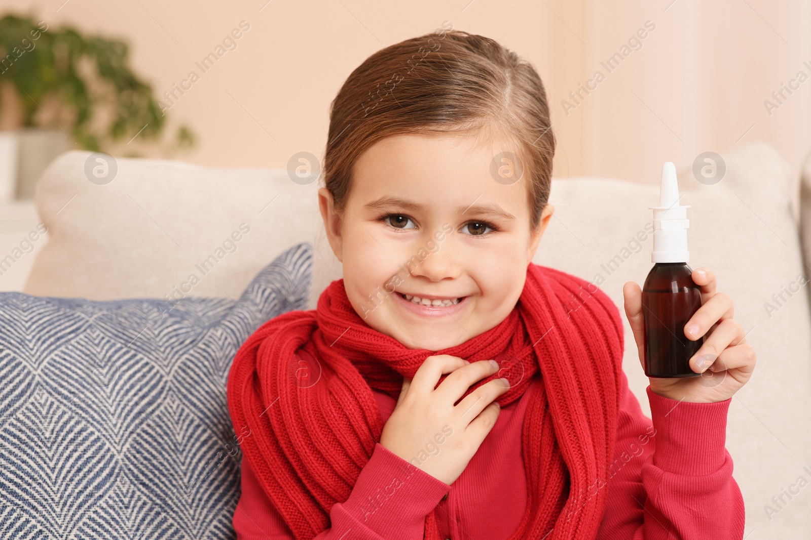 Photo of Happy little girl holding nasal spray on sofa indoors