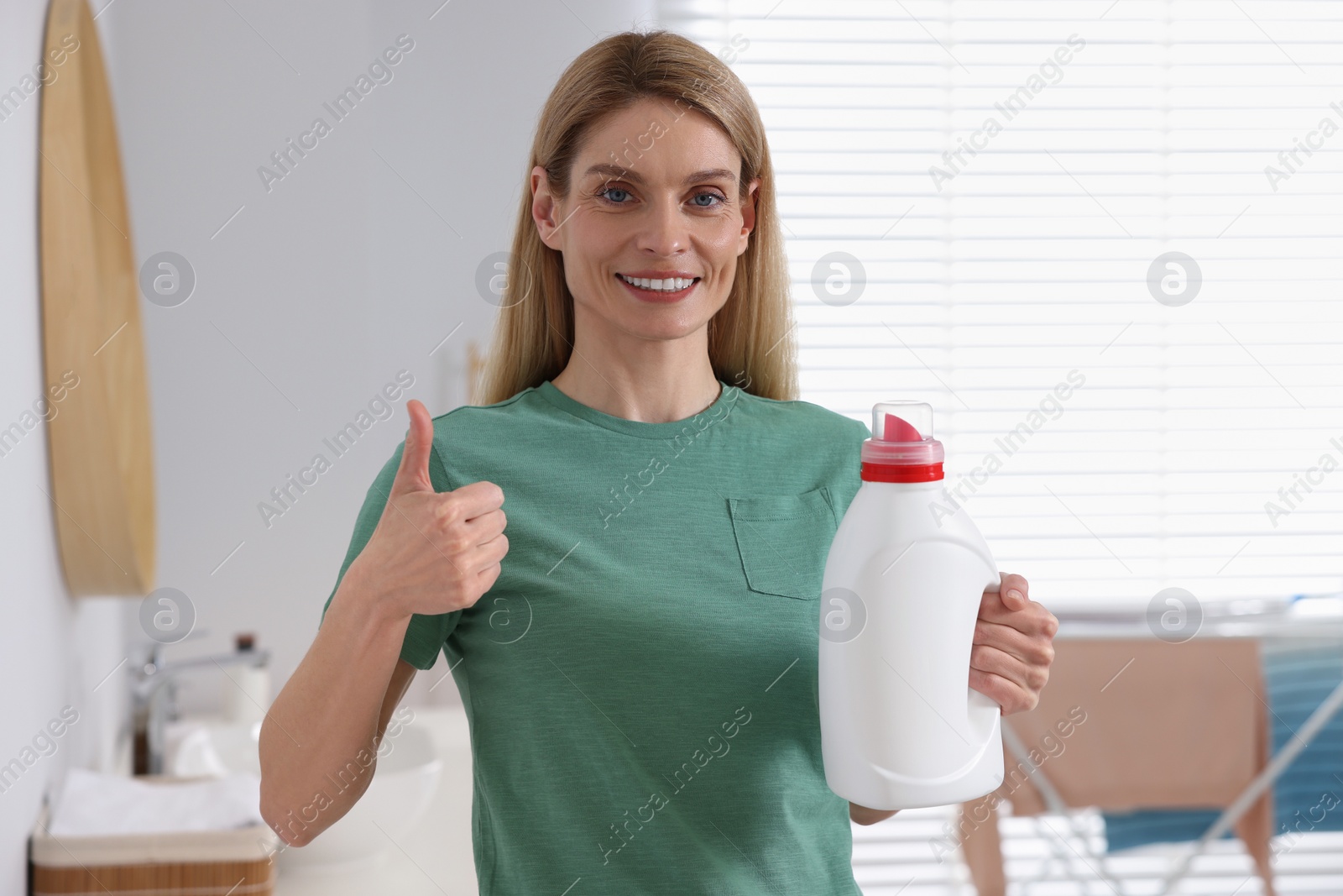 Photo of Woman holding fabric softener and showing thumbs up in bathroom