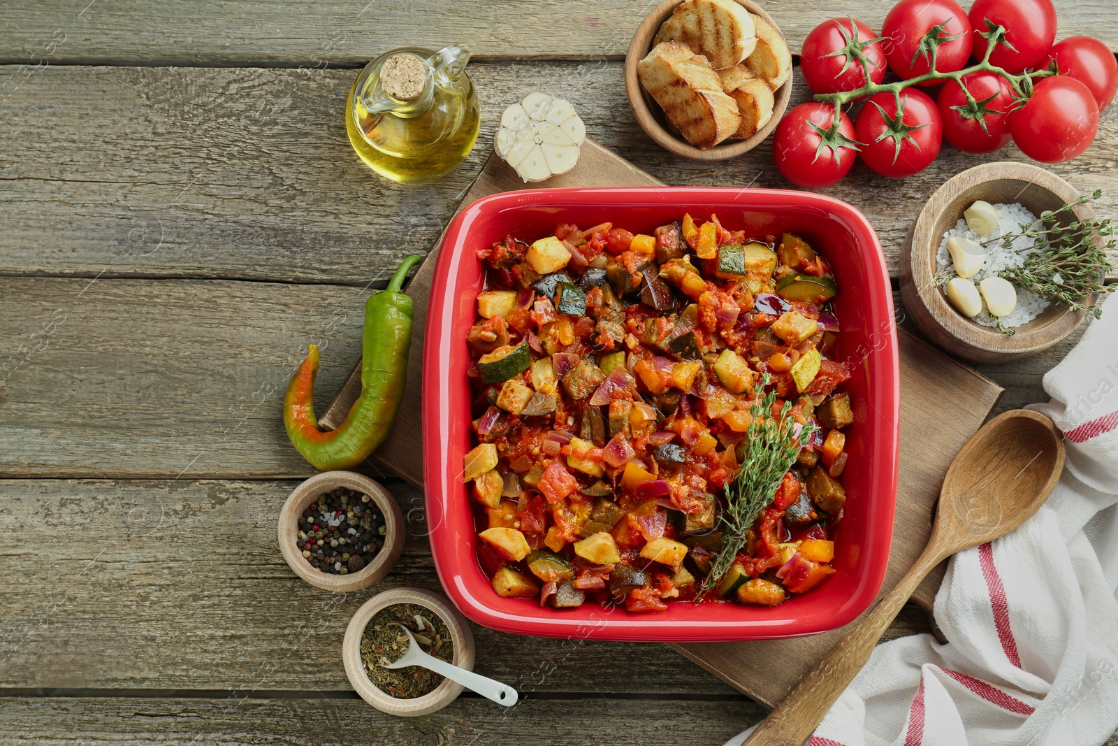 Photo of Dish with tasty ratatouille, ingredients and bread on wooden table, flat lay