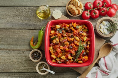 Dish with tasty ratatouille, ingredients and bread on wooden table, flat lay
