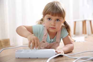 Photo of Little child playing with power strip and plug on floor indoors. Dangerous situation