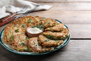 Photo of Delicious zucchini fritters with sour cream served on wooden table, closeup