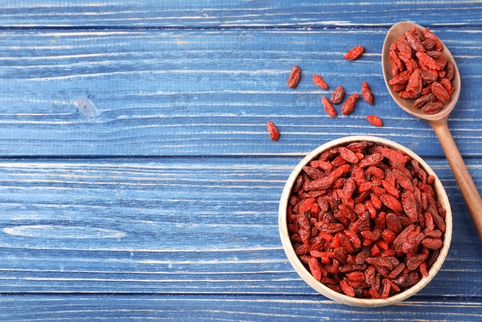 Photo of Dried goji berries on blue wooden table, flat lay. Space for text