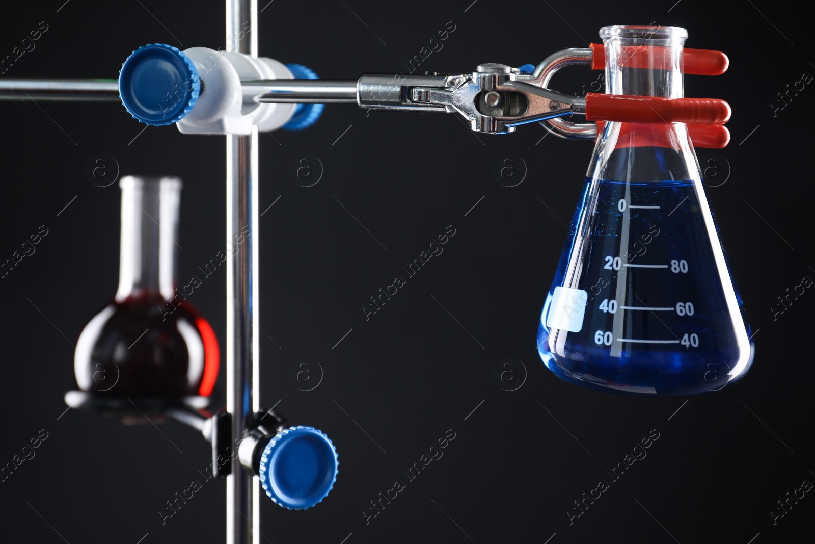 Photo of Retort stand and laboratory flasks with liquids on black background, selective focus