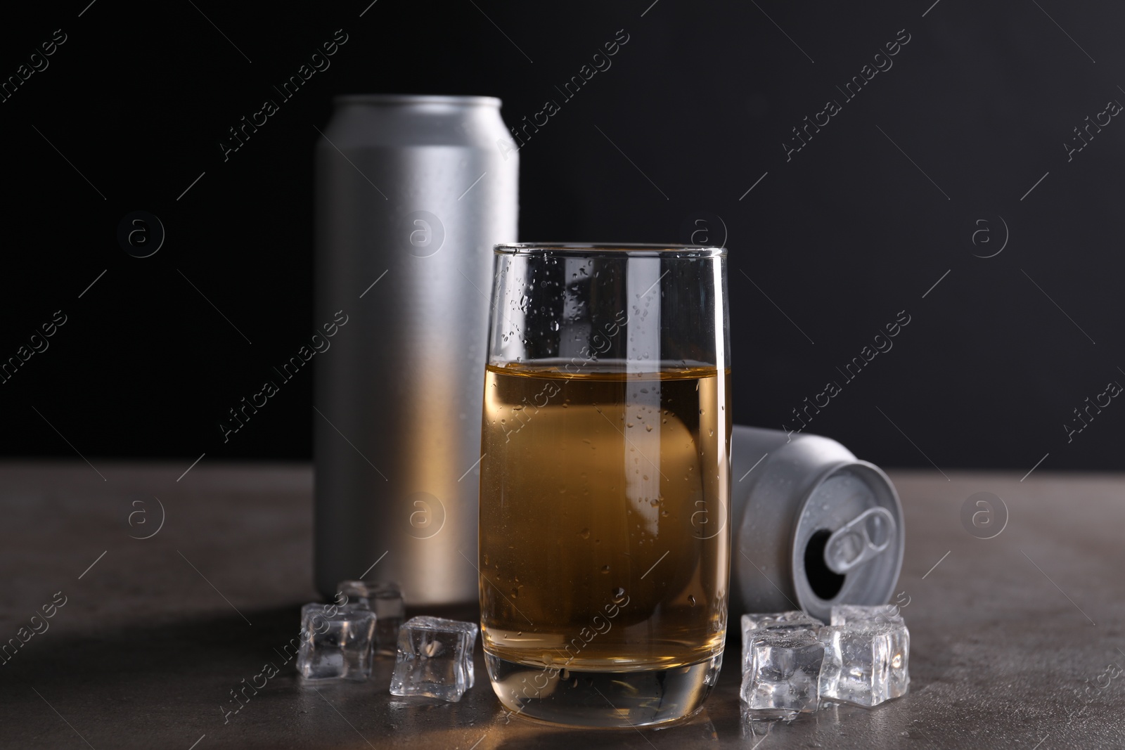 Photo of Energy drink in glass, aluminium cans and ice cubes on grey table