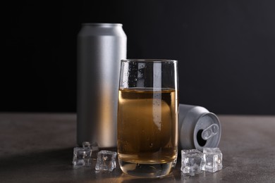 Photo of Energy drink in glass, aluminium cans and ice cubes on grey table