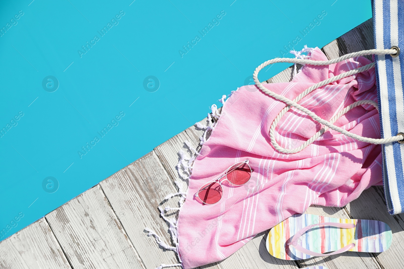 Photo of Beach accessories on wooden deck near outdoor swimming pool, flat lay. Space for text