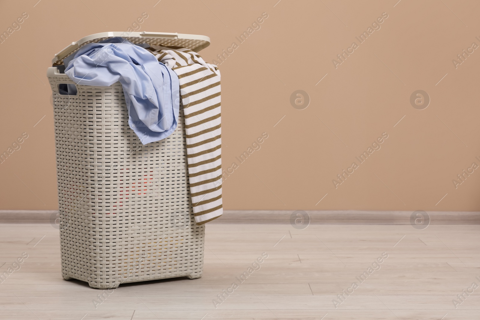 Photo of Plastic laundry basket with clothes near beige wall. Space for text