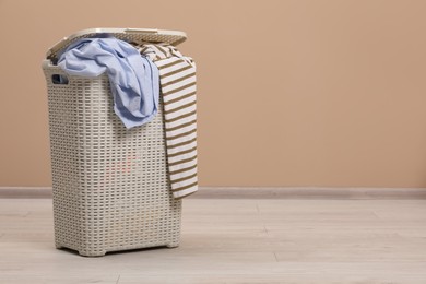 Photo of Plastic laundry basket with clothes near beige wall. Space for text