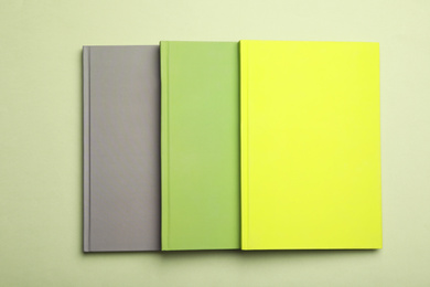 Stylish color notebooks on green background, top view