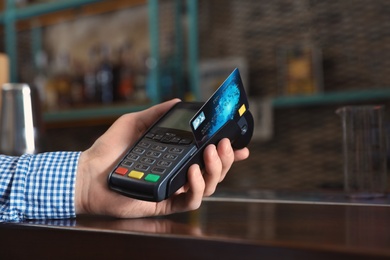 Man using credit card machine for non cash payment in cafe, closeup. Space for text