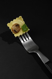 Fork with tasty ravioli and mushroom on black table, closeup