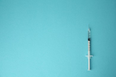 Medical syringe on light blue background, top view. Space for text