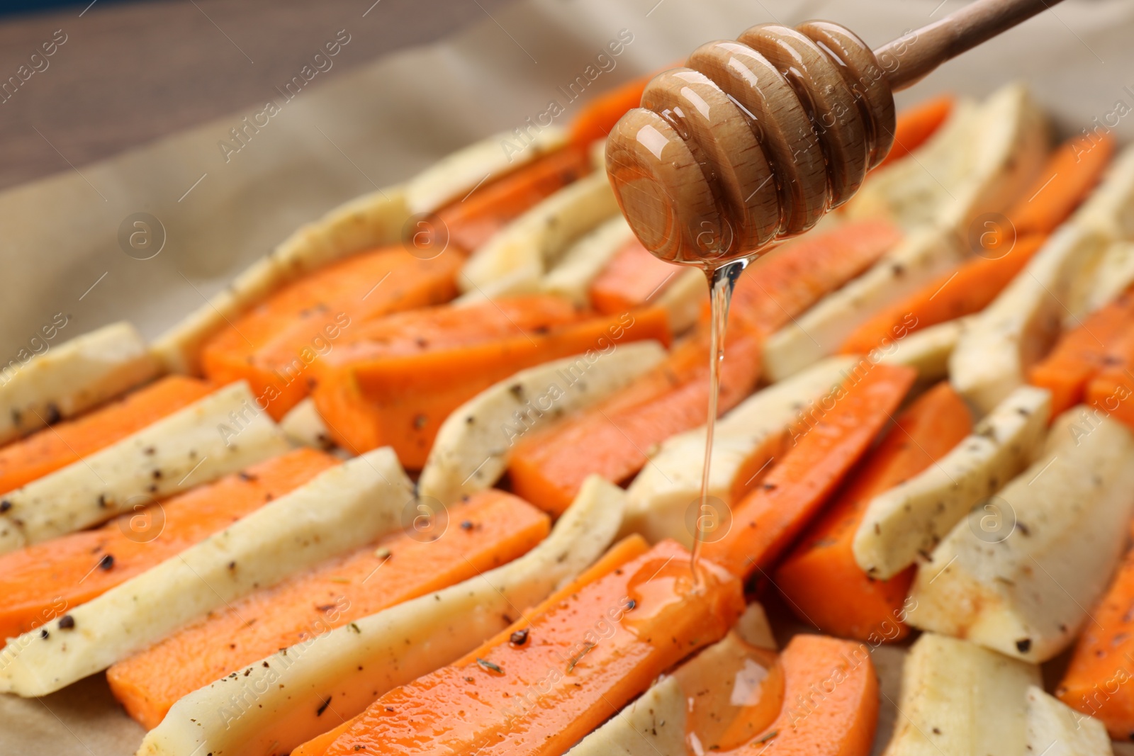 Photo of Pouring honey onto slices of parsnip and carrot, closeup