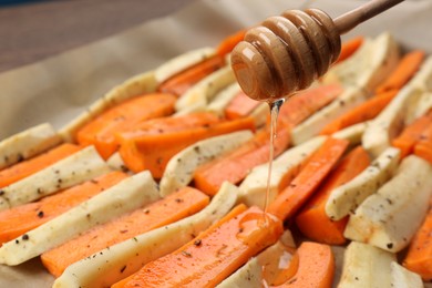 Pouring honey onto slices of parsnip and carrot, closeup