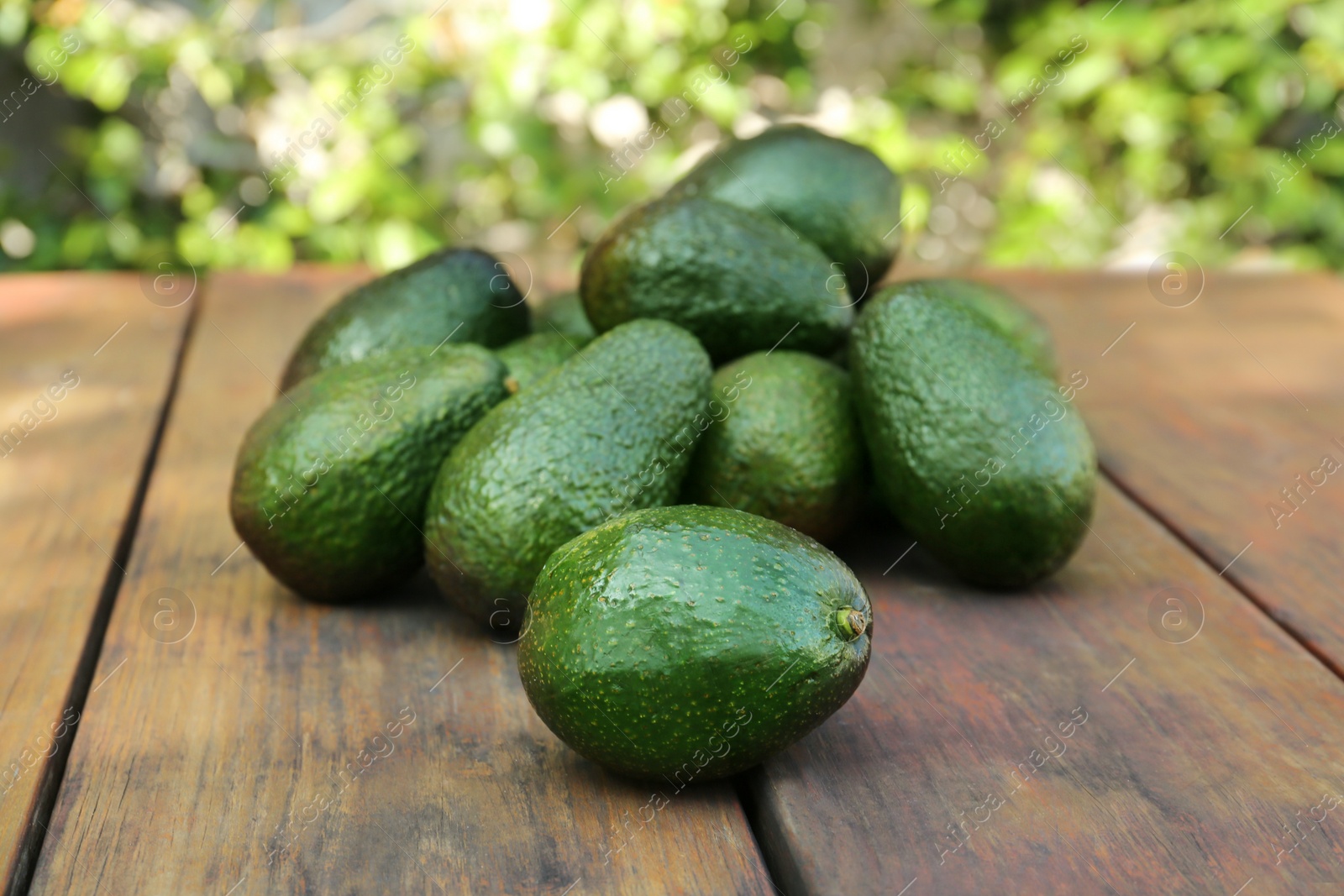 Photo of Many tasty ripe avocados on wooden table outdoors