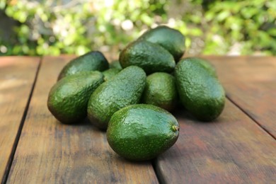 Many tasty ripe avocados on wooden table outdoors
